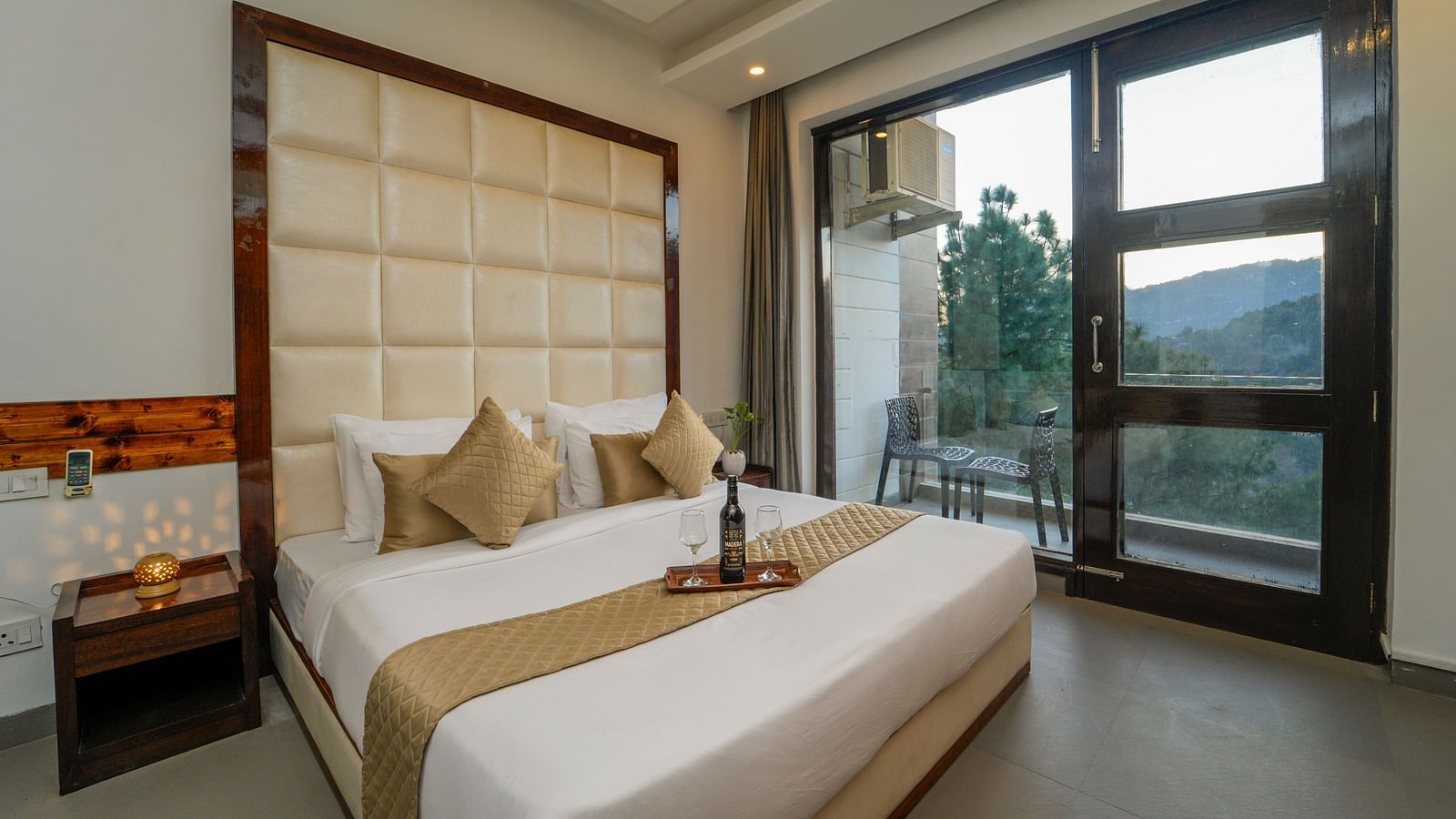 The premium room of DLS Whispering Winds with a bed, bed side tables, and a glass door leading to the balcony overlooking the mountain view